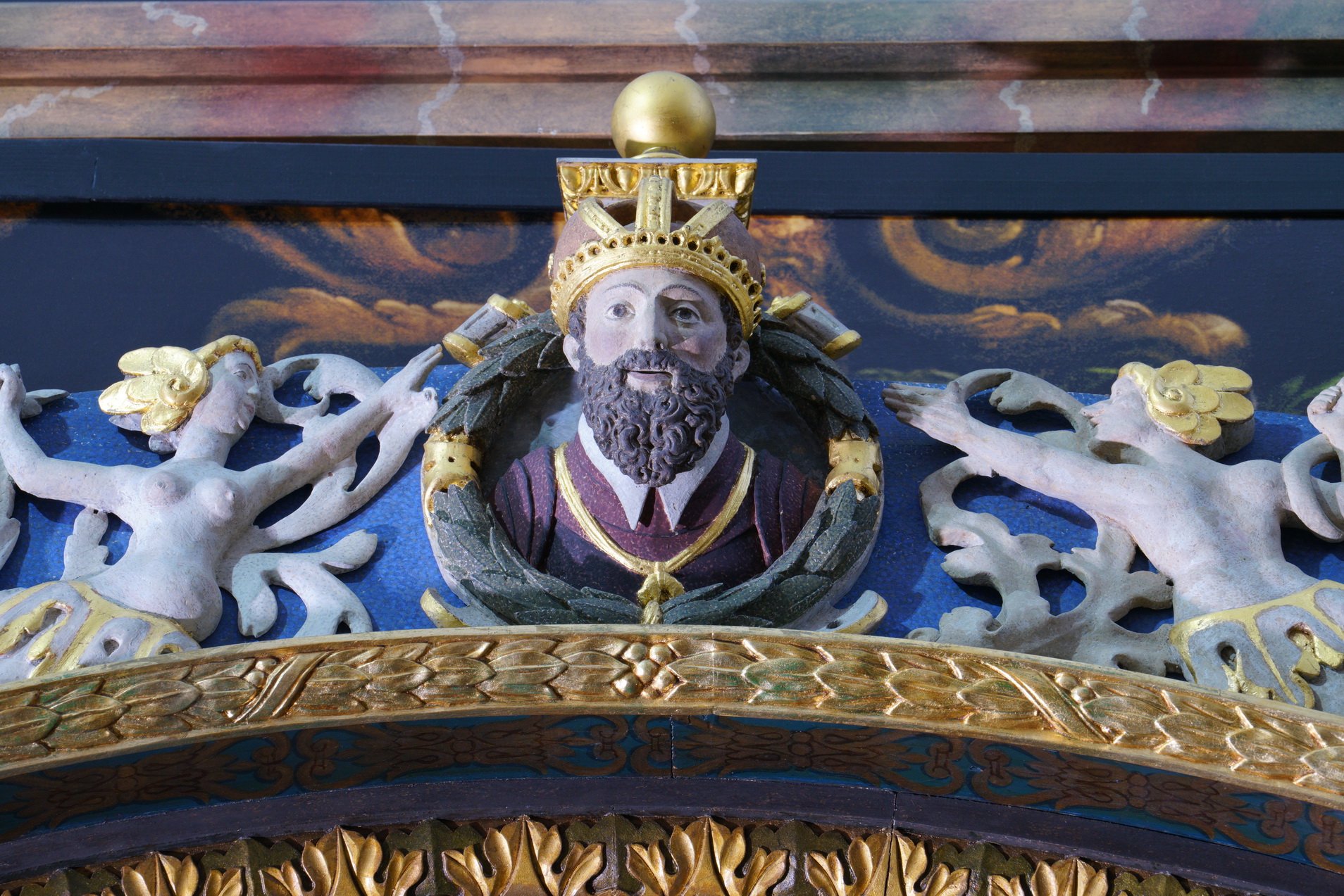 Fragment ramy obrazu „Czterech synów Hajmona na koniu Bajardzie”, zwieńczenie. Rzeźba, głowa brodatego mężczyzny, ma na głowie koronę. Wokół złocone ornamenty, postaci kobiece.