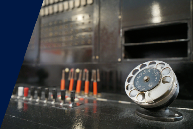 Zdjęcie. Fragment radiostacji. Czarny blat i tylnia ścianka, na nich guziki i pokrętła. Na pierwszym planie telefoniczna tarcza numerowa.